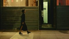 a woman walking down the street in front of a building at night with an open door