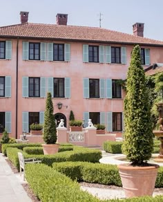 a large pink building with lots of windows and plants in the foreground, surrounded by hedges