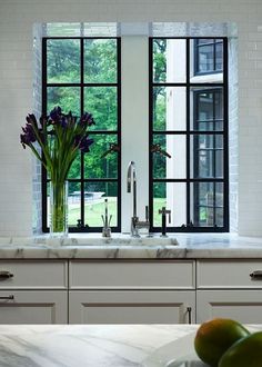 a kitchen with marble counter tops and two windows that look out onto the trees outside