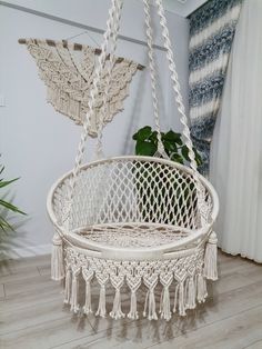 a white hanging chair with tassels on the bottom and side, in front of a window