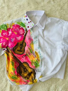 a white shirt with a guitar and pink flower on the left chest is laying on a bed