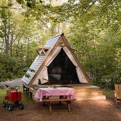 a small wooden cabin in the woods with a table and chairs on the ground next to it