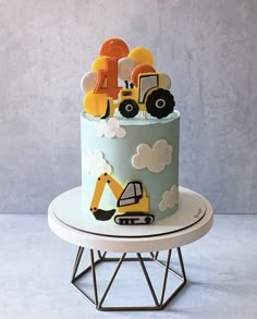 a blue cake with construction vehicles and clouds on it is sitting on top of a stand