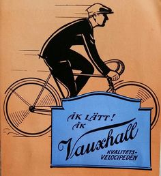 a man riding a bike down a street next to a blue and white sign with the words vaushchald written on it