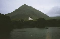 a white house sitting on top of a mountain next to a body of water with birds flying around it