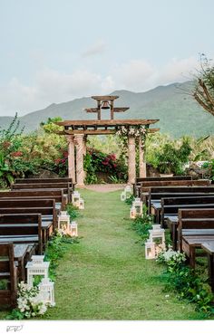 an outdoor ceremony set up with wooden chairs and candles on the aisle, surrounded by greenery