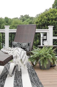 a chair and table on a deck with potted plants in the foreground, trees in the background