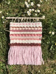 a pink and white wall hanging in the grass with daisies behind it on a stick