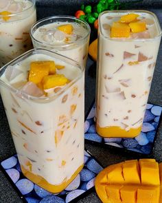 three glasses filled with fruit and ice on top of a blue place mat next to two slices of mango