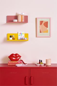 a red dresser topped with lots of different types of items next to a pink wall