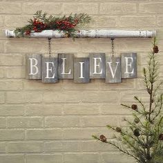 a brick wall with three wooden signs hanging from it's sides and a pine tree in the foreground