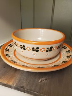 an orange and white bowl sitting on top of a wooden table next to a plate