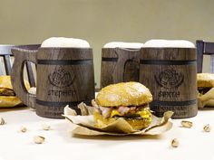 three beer mugs sitting next to each other on top of a table with food