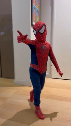 a person in a spiderman costume standing on a wooden floor with his arms out