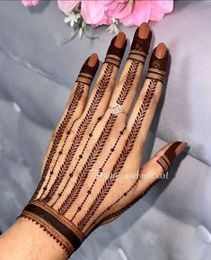 a woman's hand with henna tattoos on it and flowers in the background