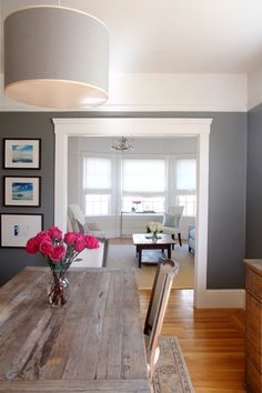 a dining room table with flowers in a vase on top of it and pictures hanging above the table