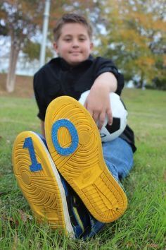 a young boy sitting in the grass with his foot on a soccer ball that is next to him