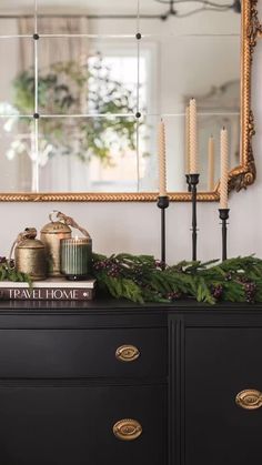 a black dresser with candles and evergreen garland on top