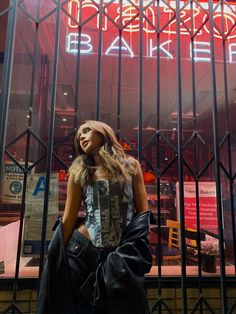 a woman standing in front of a building with a neon sign above her head and back