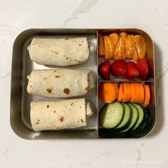 an open lunch box with fruit, vegetables and tortilla wraps on it