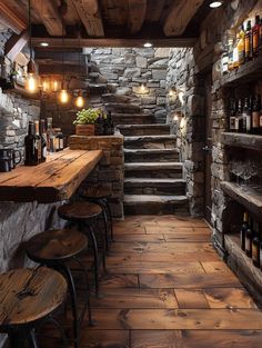 a rustic bar with stone walls and wooden steps leading up to the second floor, along with stools