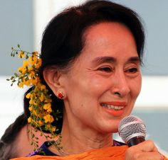 a woman holding a microphone in her right hand and wearing an orange scarf around her neck