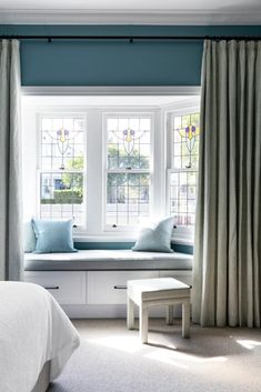 a bedroom with blue walls, white curtains and a bench in front of the window