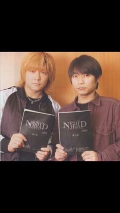 two young men standing next to each other holding up black and white books with writing on them