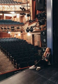 a woman sitting on the floor in front of an empty auditorium with chairs and speakers