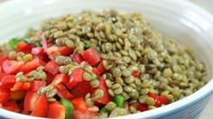 a bowl filled with lentils and tomatoes on top of a table next to a knife