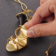 a hand is holding a gold shoe ornament on a black surface with a chain