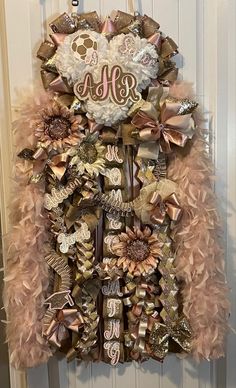 a door hanger decorated with pink and gold ribbons, flowers, and monogrammed letters