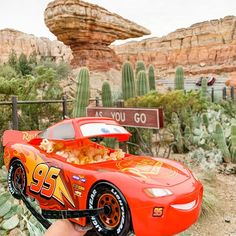 a hand is holding a toy car in front of a desert area with cacti