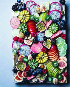 an art work made out of fruits and vegetables on a blue surface with blackberries, kiwis, raspberries, oranges, lemons, limes