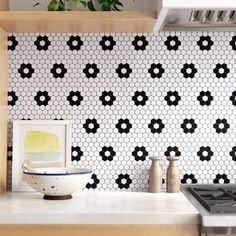 black and white tiles are on the wall behind a stove top in a kitchen with wooden cabinets