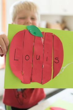 a child holding up a piece of paper with the word louis cut out of it