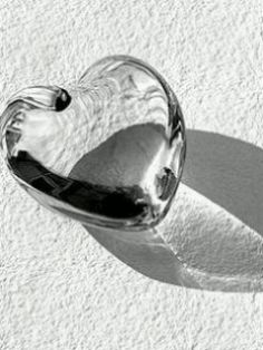 a heart shaped glass object sitting on top of a white surface with the shadow of it