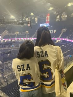 two women sitting in the bleachers at a hockey game wearing white and blue jerseys