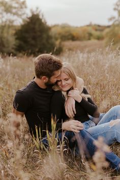 a man and woman are sitting in the tall grass hugging each other while they smile