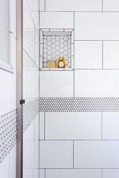 a white tiled shower stall with yellow items on the shelf and in the corner next to it