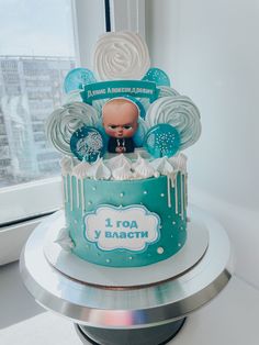 a baby's first birthday cake decorated with blue and white icing on a table in front of a window