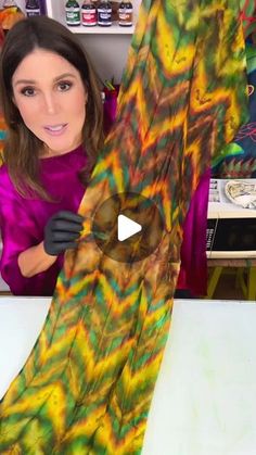 a woman is holding up a piece of art that looks like a tie - dyed scarf