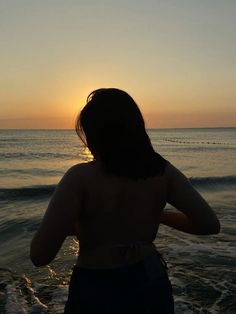 a woman standing on top of a sandy beach next to the ocean at sun set