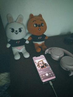 two stuffed animals sitting next to each other near a cell phone and headphones on a table