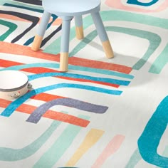 a colorful rug with various shapes and colors on the floor next to a small stool