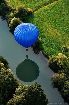 a hot air balloon floating over a river in the middle of a lush green field