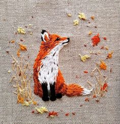 an embroidered picture of a fox sitting on the ground with autumn leaves all over it