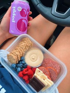 a person is holding a can of soda and some food in their lap while driving