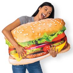 a woman is holding a giant hamburger pillow