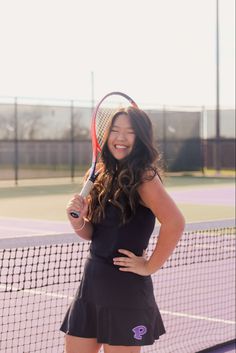 a young woman holding a tennis racquet on top of a tennis court in front of a net